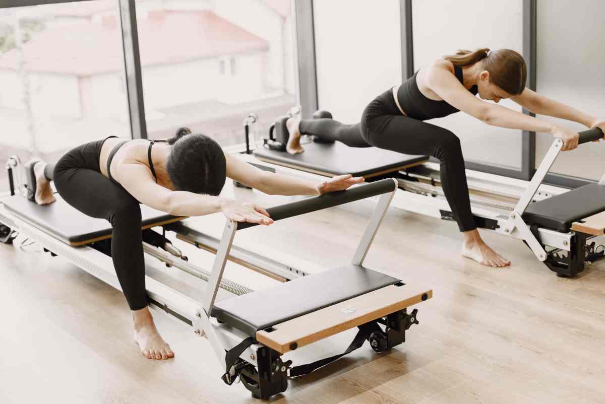 Two girls in a bright gym doing duet stretching with equipment benefits of pilates